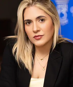 Dra. Caroline Bandeira sentada em uma poltrona no escritório, com o logo do escritório na tela ao fundo
