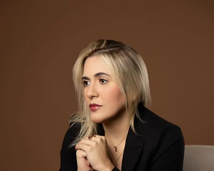 Dra. Caroline Bandeira, sentada, com as mãos juntas sob o queixo, olhando para o lado