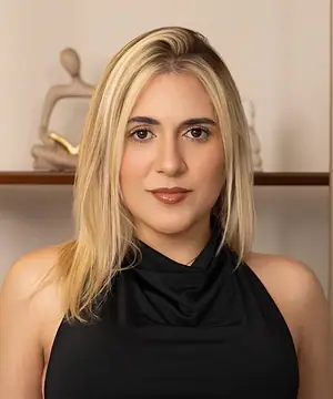 Dra. Caroline Bandeira, de conjunto preto, em pé diante de uma estante