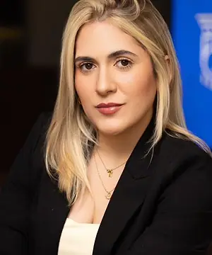Dra. Caroline Bandeira sentada no escritório, com as mãos sobre os joelhos e o logo na tela ao fundo