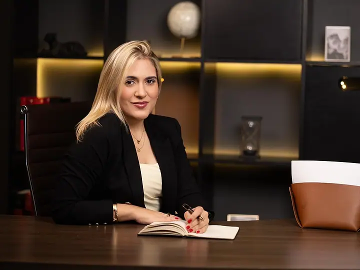 Dra. Caroline Bandeira sorrindo à mesa do escritório, com um caderno aberto