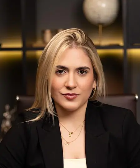 Dra. Caroline Bandeira à mesa do escritório, com as mãos juntas, olhando para a câmera