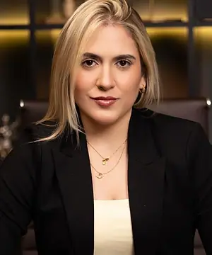 Dra. Caroline Bandeira à mesa do escritório, com as mãos juntas, olhando para a câmera